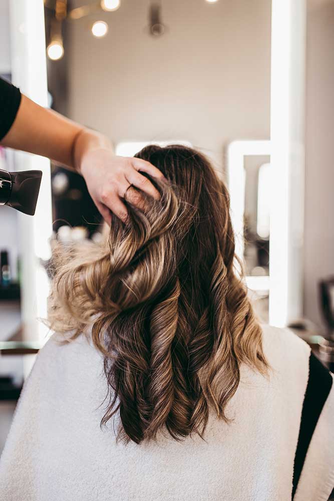 Seitenansicht einer Friseurin, die Haarspray verwendet, um die weiblichen Haare des Kunden in einem Friseursalon zu fixieren